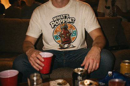 What’s Poppin’ graphic tee with retro bottle character on ivory shirt, queer nightlife inspired design