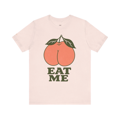 Soft Pink EAT ME graphic tee with oversized coral peach and dark olive retro lettering.