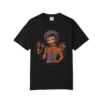 Black vintage-style tee featuring a retro pop-art illustration of a glamorous masculine figure with a TV head, dusty lavender teased wig, visible smiling mouth, rhinestone jewelry, and an off-shoulder lavender gown at an upscale 1980s cocktail party. Muscular masculine body with broad shoulders and chest hair, rendered in muted lavender, plum, cream, and black with halftone comic texture. Small text below reads: “still fabulous.”